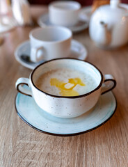 A beautiful white plate with oatmeal porridge and butter on the table. Perfect breakfast in the city cafe with oatmeal, coffee and tea on the round wooden table.