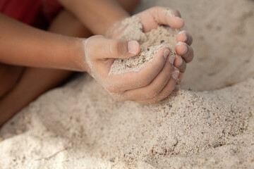 Boy holding sand in hands at the beach in summer time, family vacation concept
