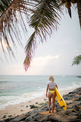 Rear view of a woman in a white cropped t-shirt with a yellow surfboard on the ocean.