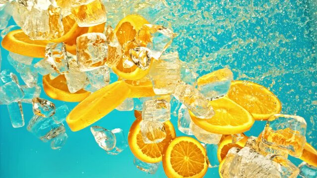 Citrus orange slices and ice fall or explode in super slow motion 1000fps on blue background.Juicy sweet orange and fly ice cube or water splash or pouring drops juice in super slow motion on 1000fps