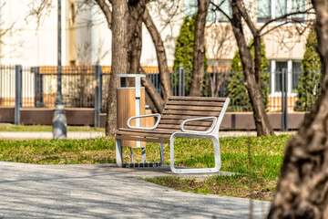 Bench in the park near the walking path among the trees on a sunny spring day.