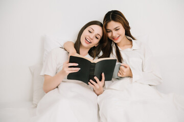 Attractive lesbian couple use mobile phone, tablet watch movie on bed. Beautiful sibling in pajamas...