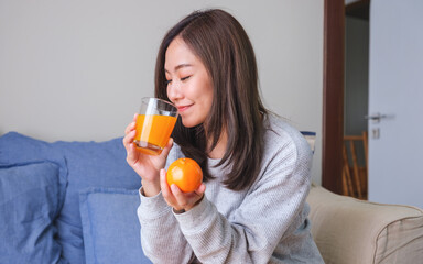 Portrait image of a young woman holding an orange and drinking fresh orange juice at home