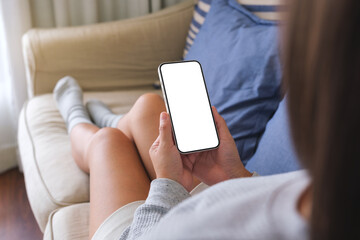 Mockup image of a woman holding mobile phone with blank desktop white screen while lying on a sofa at home