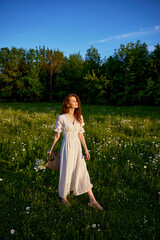 a beautiful woman in a light, light, summer dress is standing in a flowering meadow in the sunset light