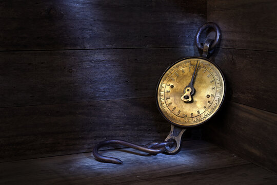 Antique, spring balance, brass face, weighing scale with a hook in a dark, rustic wooden setting, mood lighting, copy space 