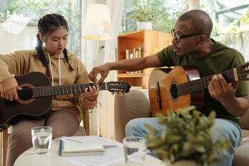 Tutor explaining teenage girl how to hold guitar