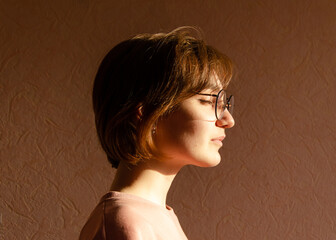 Portrait of a beautiful young woman with round glasses, face turned to the sun, eyes closed. The...