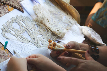 Close-up photo of a woman and a girl making lace using bobbins