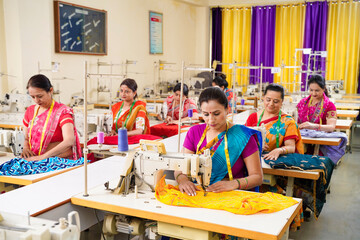 Indian women group working on sewing machine at textile factory.