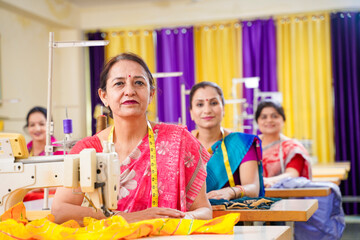 Indian women group working on sewing machine at textile factory.