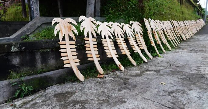 Identical wooden blanks for ornamental signs in shape of palm tree with arrow-plates for words, stand in row in street next to wall of building. Various types of handicrafts, from highly artistic to
