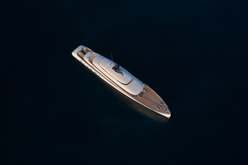 Innovative white big yacht anchored in the morning sun top view. Mega yacht on a dark background aerial view.