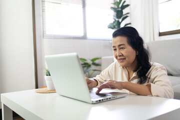 Middle age Asian woman Work from home. senior woman smiling Beautiful mature asian woman on laptop with technology concept