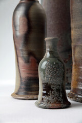 Close up shot of handmade ceramic bottle with larger bottles in the background - brown colored - on white background