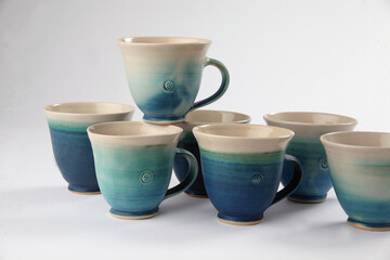 A cluster of ceramic handmade coffee or tea cups - one cup placed on top of the others on white background