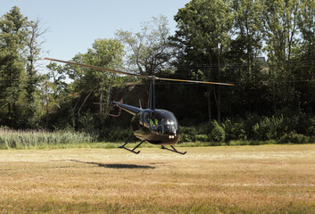 A small helicopter landing on the ground of a field with forest background - in Norway - mid day light