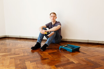 man varnishes oak parquet with a roller during renovation