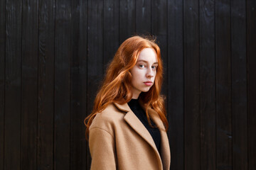 Fototapeta premium young stylish red-haired woman in a coat near her house in autumn