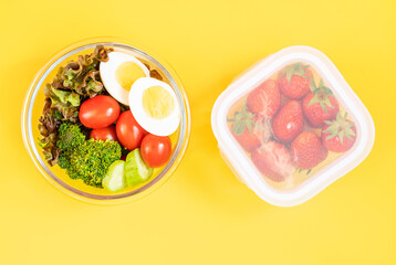 Fototapeta na wymiar Healthy food in glass lunch boxes on yellow background close-up, top view.