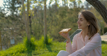Girl eating sandwich with peanut butter in the park and relaxing on the grass