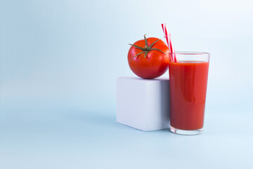 Tomato juice in a transparent glass and a juicy tomato on a light background.