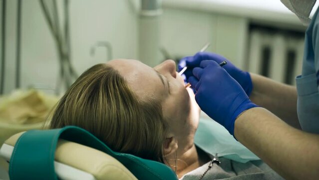 A doctor examines a woman's teeth with a dental instrument. Close-up