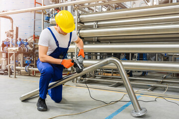 Factory worker in yellow hard hat operate with stainless steel pipe sander polishing machines....