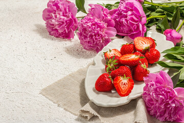 Sweet ripe strawberries and fragrant peonies bouquet. Summer plaster background, seasonal design