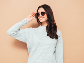 Young beautiful smiling female in trendy summer jeans and sweater clothes. Sexy carefree woman posing near beige wall in studio. Positive model isolated. Cheerful and happy. In sunglasses