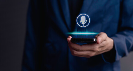 businessman using utilizes his smartphone as an AI assistant, effectively issuing voice commands through its microphone symbol, enhancing productivity with cutting-edge technology. - obrazy, fototapety, plakaty