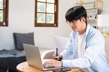 Fototapeta premium An Asian young business man work from home using computer and notebook together to manage his financial status