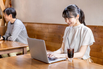 カフェでコーヒーを飲みながらリモートワークするアジア人女性
