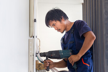 Man with hammer drill making hole in wall, Technician man installing an air conditioning in a client house, Young repairman fixing air conditioner unit, Maintenance and repairing concepts