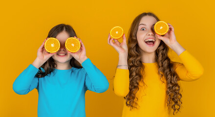 cheerful teen girls hold orange fruit on yellow background