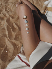 Beautiful young woman sunbathes on the beach. Female leg with seashells. Sexy female body. Minimal...