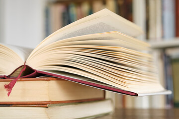Naklejka premium Open book or textbook on a pile of closed books in front of a bookcase in a library. Education learning concept. Image with selective focus.