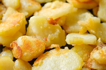 Closeup of yellow fried or baked potatoes with a crispy brown crust. Image with selective focus.	
