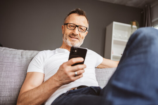 Middle-aged man relaxing on sofa and using smartphone