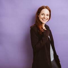 Red-haired 30-year-old woman standing in front of a violet background and smiling