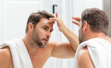 Beauty face portrait of a beautiful man applying face cream. Moisturizing skincare cream for man. Mask, skin lifting and anti-aging effect. Beauty male face concept. Skincare and aging. Face cosmetic. - Powered by Adobe