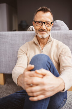 Happy and Relaxed 50s Man Sitting Comfortably on Living Room Floor with Glasses