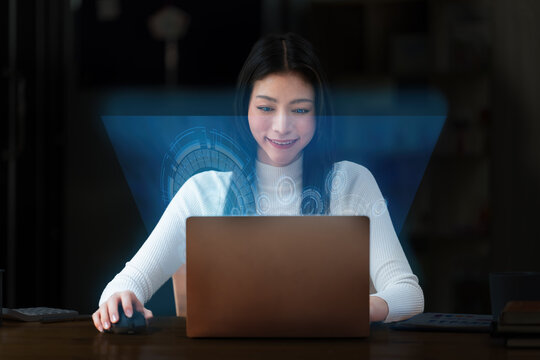 Portrait of an Asian businesswoman in a casual suit using a technology laptop for working via futuristic screen hologram in a modern office, Business owner and entrepreneur concept.