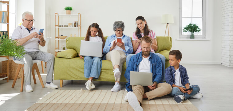 Big Family Watching Gadgets While Sitting On Sofa At Home. Grandparents, Dad, Mom, Daughter And Son Using Digital Devices, Everyone Using Their Own Gadget. Social Networks Dependence Concept