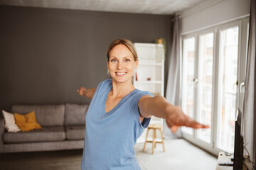Young blonde woman practicing yoga in her apartment and smiling at the camera