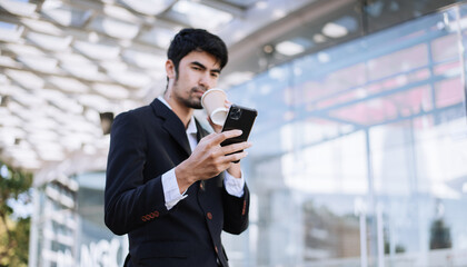 Professional businessman using digital tablet, smartphone and holding coffee to go while working at office