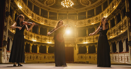 Portrait of a Group of Female Violinists Playing Violins While on the Stage of an Empty Classic...
