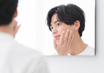 メンズビューティー/鏡を見ながらスキンケアをする若い男性