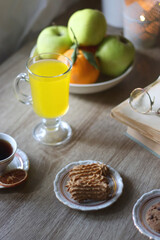 Cup of tea, plates with cookies, glass of orange juice, books, reading glasses, bowl of fruit and candles on the table. Selective focus.