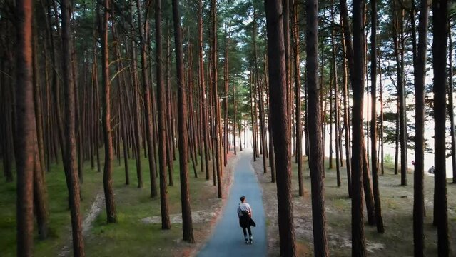 drone shot of man rollerblading on the running track through the forest during sunset along the beach